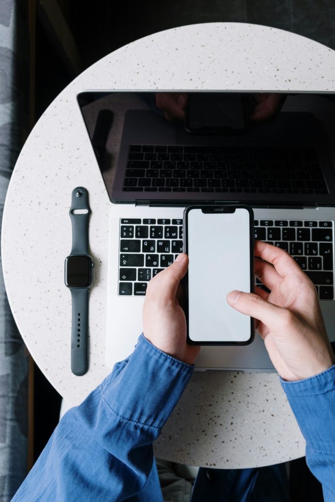 pexels-photo-5054352-5054352 Top view of a person using a smartphone above a laptop with a smartwatch on the table.